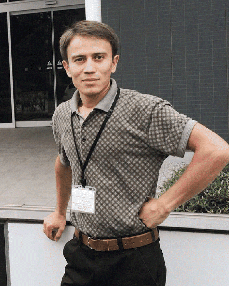 Professional headshot of Uzbek man in his 40s with short dark hair wearing navy blue suit and tie in modern office setting